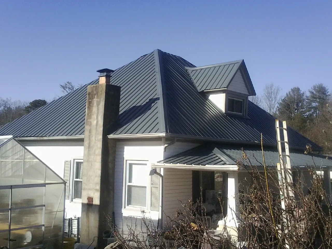 Dark blue standing seam metal roof on a white farmhouse with dormer — Slate & Tile Roof Repair by Roofing Brothers in Alva