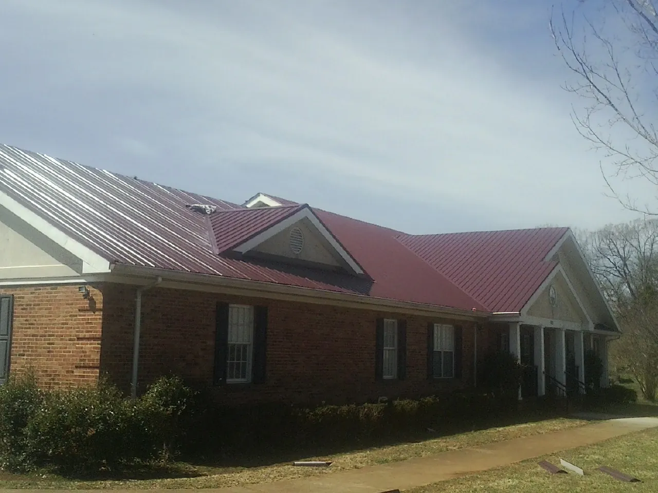 Red metal roof with gabled entries on a long brick building, from a Hail Damage Roof Repair job in Alva