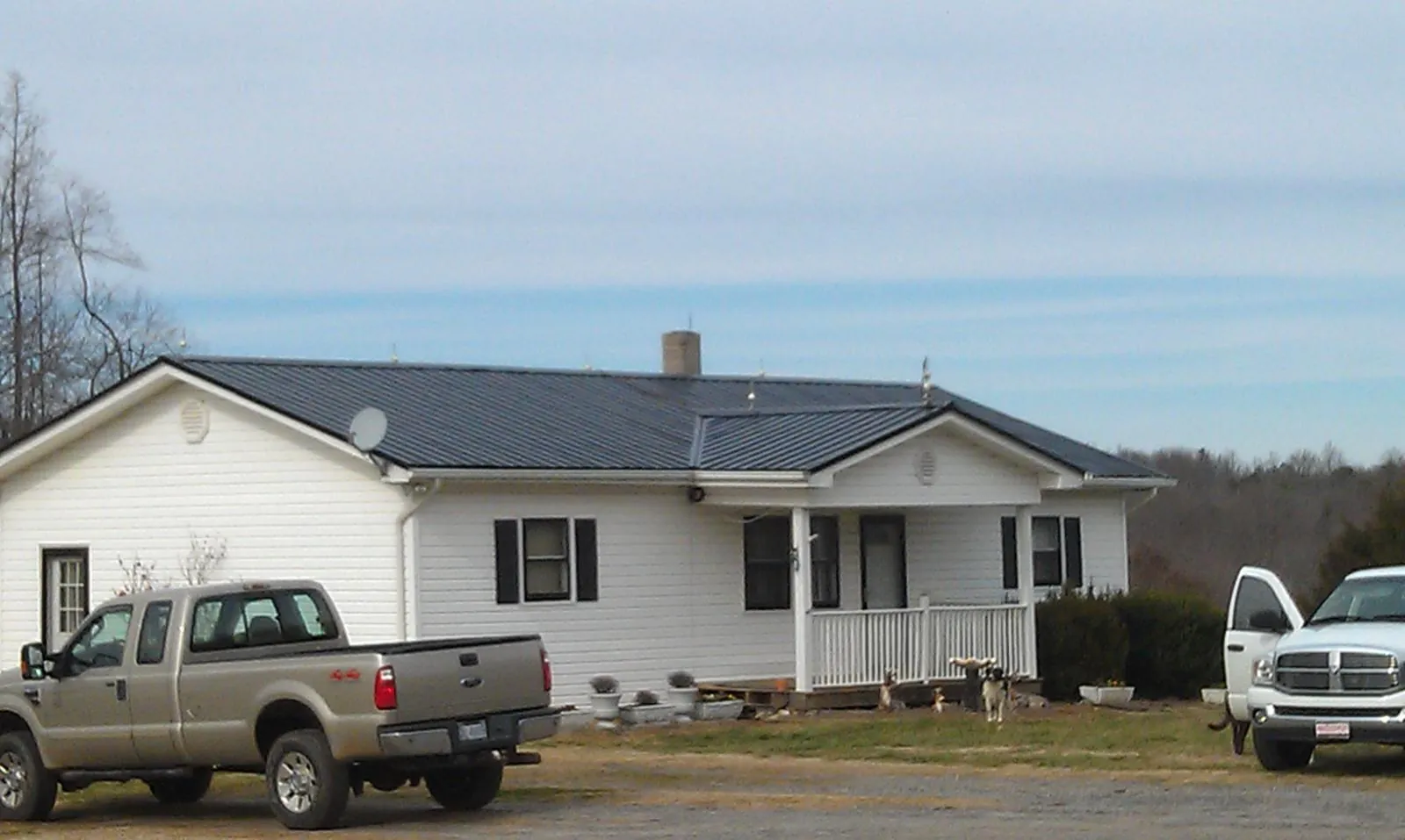 Finished dark metal roof on a white ranch home with work trucks parked in Alva